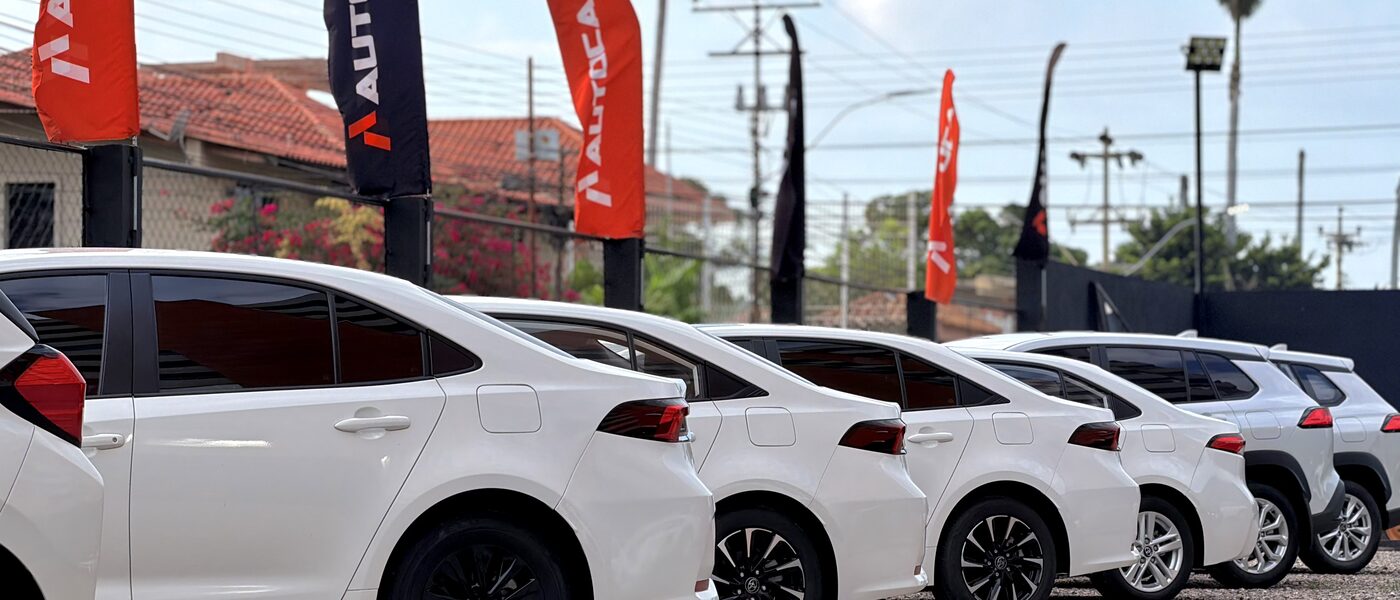 Lote de AUTOCA en Lechería con banderas de la marca y vehículos nuevos en fila